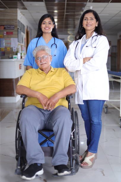 Indian Nurse looking very happy greeting a senior patient in a wheelchair at the hospital and smiling - healthcare concepts.